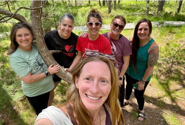 Alissa taking a selfie with five smiling retreat participants gathered around a pine tree